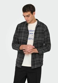 Zwart en grijs geruit overhemd met knoopsluiting aan de voorkant en lange mouwen, gedragen over een lichtgekleurde graphic t-shirt. Soepele stofstructuur.