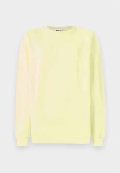 Lys gul sweatshirt lavet af bomuld, med lange ærmer, rund hals og ribbet kant. "STIEGLITZ" præget på forsiden.