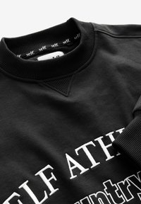 Felpa nera a girocollo con colletto e polsini a coste, caratterizzata da testo ricamato bianco che inizia con "SELF ATH" e nastro interno del colletto che legge "self."