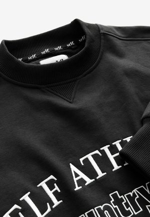 Black crewneck sweatshirt with ribbed collar and cuffs, featuring white embroidered text starting with "SELF ATH" and inner collar tape reading "self."