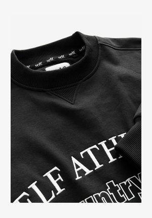 Schwarzer Rundausschnitt-Pullover mit geripptem Kragen und Bündchen, mit weißem gesticktem Text, der mit "SELF ATH" beginnt, und einem inneren Kragenband, auf dem "self." steht.