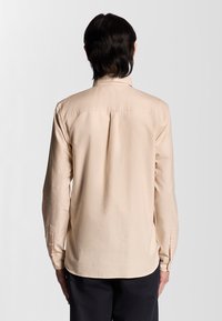 Lichtbeige lange mouwen shirt van glad stof, met een klassieke kraag, een rugplooiafwerking en knoopmanchetten. Getailleerde pasvorm.