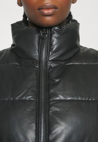 Svart vadderad jacka med hög krage, med en frontdragkedja och en slät, glänsande syntetläderyta.