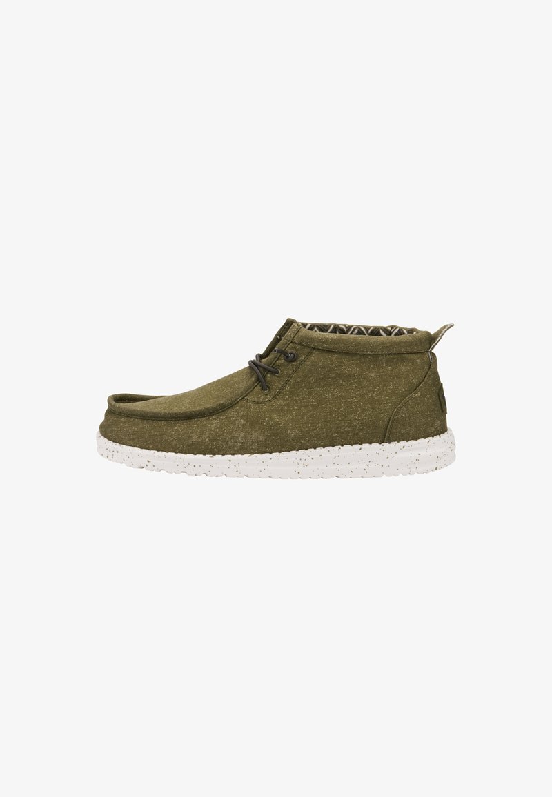 Zapatillas informales de color verde oliva con una parte superior de tela texturada, suela moteada blanca y cordones marrones, que presentan un diseño de corte bajo y un forro estampado.