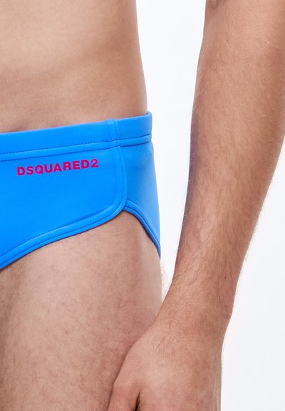 Μπλε μαγιό σλιπ από ελαστικό ύφασμα με αντίθετη ραφή και κόκκινο λογότυπο. Ο σχεδιασμός διαθέτει χαμηλή μέση και ομαλή υφή.