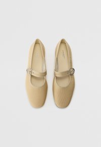Zapatos Mary Jane beige con un empeine de tela suave, punta redonda y tacón plano, que cuentan con una sola correa ajustable y hebilla plateada.