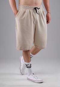 Beige shorts made from soft fabric, featuring an elastic waistband with black drawstring, side pockets, and a relaxed fit.