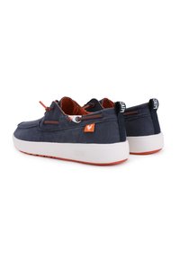 Baskets en toile marine avec semelle blanche et accents orange. Les caractéristiques incluent des œillets, un patch logo et des languettes sur le talon.
