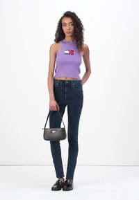 Purple ribbed sleeveless crop top with a logo patch, denim skinny jeans, black handbag with a logo, and shiny black loafers.