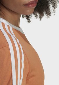 Orange athletic shirt featuring white stripes on the shoulders. It has a round neckline and a soft texture.