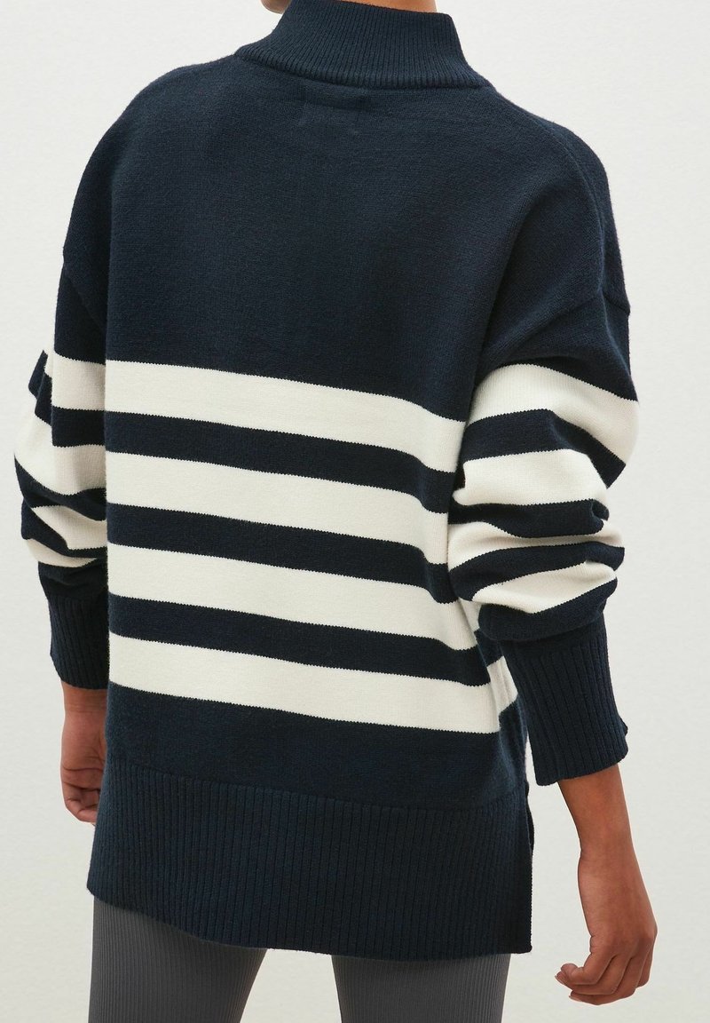 Pull à rayures bleu marine et blanches avec un col montant, une coupe oversize, des poignets côtelés et des fentes latérales à l'ourlet. Texture en tricot doux.