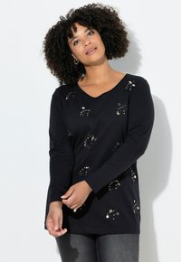 Zwarte top met lange mouwen van zachte stof, voorzien van metalen stippen in een verspreid patroon op de voorkant en een ronde halslijn.