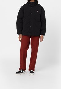 Svart kviltad jacka med hög krage och tryckknappar, i kombination med vinröda byxor och svarta sneakers. Har en mjuk textur och en avslappnad passform.