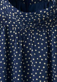 Navy blue fabric with white polka dots forming a gathered pattern around a dress neckline and bodice.