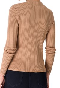 Personne portant un pull beige ajusté à manches longues et côtelé, associé à un jean bleu foncé, vue de dos.