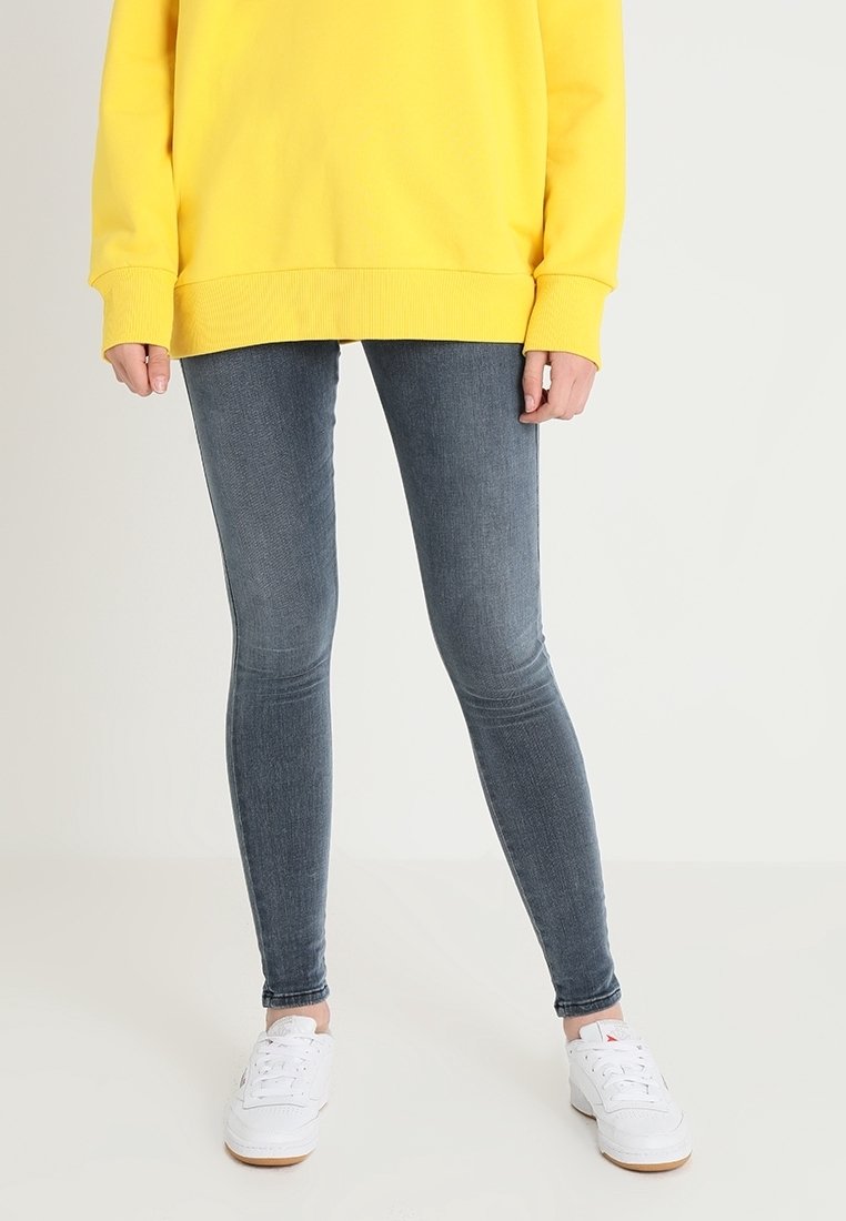 Yellow oversized sweatshirt, slim gray jeans, white sneakers. The outfit features a relaxed fit and smooth textures with minimal detailing.