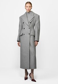 Szary dwunapiersiowy płaszcz z dużymi klapami, z dwoma przednimi kieszeniami, o długiej sylwetce i teksturowanej tkaninie.