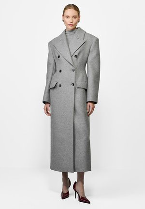 Šedý dvouřadý kabát s velkými klopami, který má dvě přední kapsy, dlouhý siluetu a strukturovanou tkaninu.
