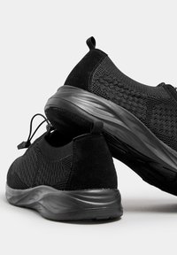 Zwarte sportieve schoenen met een bovenwerk van gestructureerd mesh en gladde synthetische accenten. Voorzien van een flexibele zool en een trekband aan de hiel.