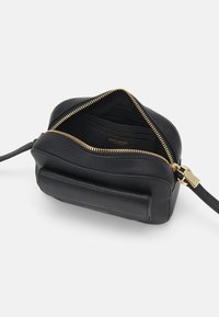 Černá kožená kabelka s texturovaným povrchem, zlatým zipem a vnitřními sloty na karty. Kompaktní tvar s odnímatelným popruhem.
