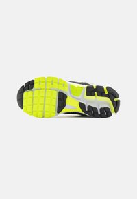 Black and yellow running shoe sole with textured traction pattern, featuring neon yellow segments and black rubber accents for grip.