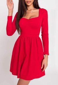 Czerwona sukienka z długim rękawem i kwadratowym dekoltem, z detalem marszczenia przy biuście i rozkloszowanym dołem, wykonana z gładkiego, elastycznego materiału.