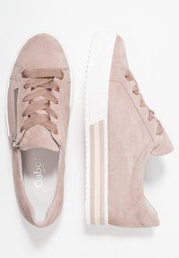 Jasnoróżowe zamszowe trampki z białymi gumowymi podeszwami, wyposażone w sznurowanie, boczny zamek oraz subtelne paski na pięcie.