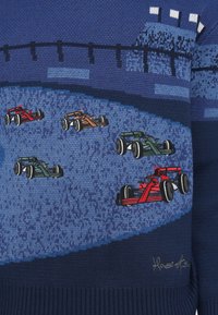 Πλεκτό πουλόβερ με μπλε διαβαθμίσεις και κεντημένα αγωνιστικά αυτοκίνητα σε κόκκινο, πράσινο και πορτοκαλί. Υφή πλέξης με ριμπ μανσέτες και τελείωμα.