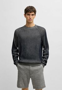 Navyblauer Strickpullover mit feinen vertikalen Streifen, geripptem Rundhalsausschnitt und Bündchen; kombiniert mit hellgrauen Shorts, die einen lässigen Stil zeigen.