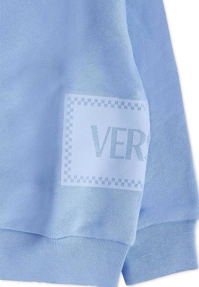 Maglione azzurro chiaro con una toppa testurizzata con la parola "VERS" circondata da un bordo quadrato. Tessuto a maglia morbido con polsini a costine.