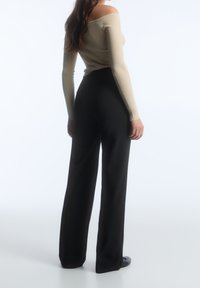 Haut beige côtelé sans épaule associé à un pantalon noir à jambes larges taille haute. Texture lisse avec une silhouette ajustée. Couleur unie sans motifs.