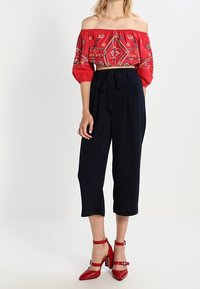 Röd off-shoulder broderad topp med korta puffärmar, kombinerad med högmidjade marinblå cropped byxor och röda klacksandaler.