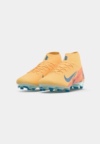 Een paar oranje Nike voetbalschoenen met hoge bovenkant, blauwe accenten en gestoken zolen op een witte achtergrond.