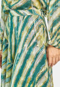 Vestido de patrones verdes y azules con rayas en espiral en diferentes tonos, confeccionado en una tela ligera con una textura sutil.