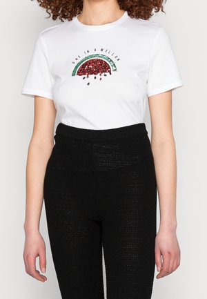Mujer con camiseta blanca con gráfico de sandía de lentejuelas y la frase "One in a Mellon,", combinada con pantalones negros de tiro alto.