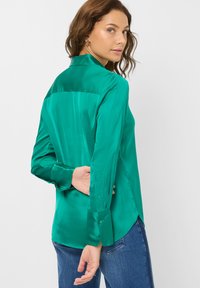 Grünseidenbluse mit strukturiertem Kragen, langen Ärmeln, Knopfmanschetten und einer glatten, glänzenden Textur. Hat einen gesplitteten Saum auf der Rückseite.