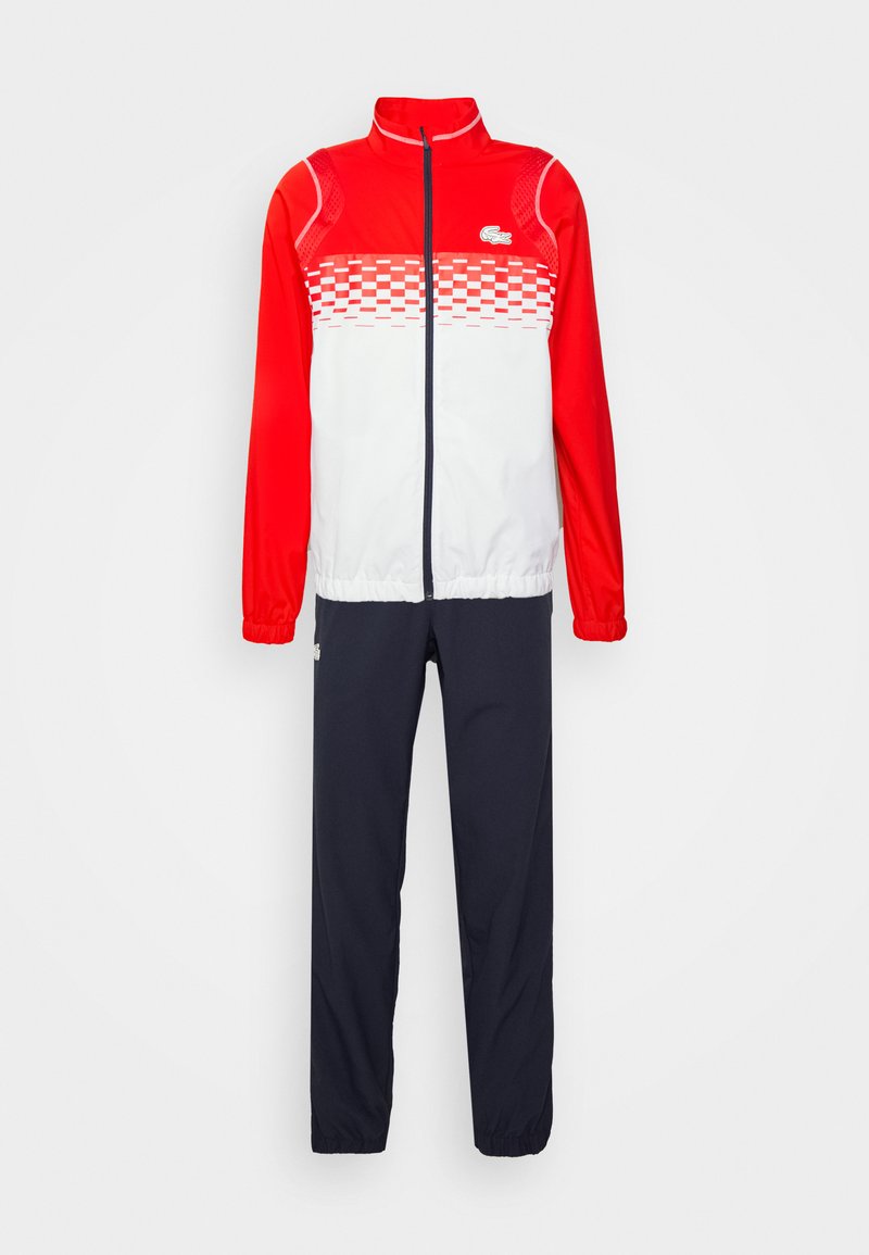 Giacca rossa e bianca con motivo a scacchi sul petto, abbinata a pantaloni blu scuro. Realizzata in materiale leggero e morbido.