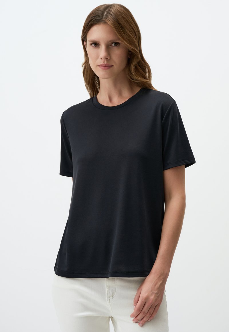 T-shirt nera a maniche corte realizzata in tessuto morbido, con scollatura rotonda classica e vestibilità comoda, indossata con pantaloni bianchi.