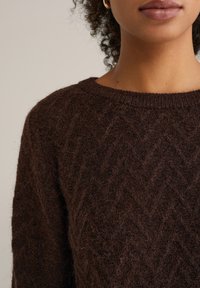 Rjavi pleteni pulover s cikcak vzorcem, z rebrastim okroglim ovratnikom in mehkim, teksturiranim zaključkom.