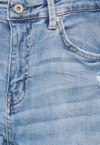 Jean en denim bleu clair avec bouton en métal, poche avant, passants pour ceinture et détails de couture orange visibles.