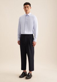 Lichtblauw overhemd met kraag en lange mouwen, zwarte tapered broek en zwarte veterschoenen. Soepele stof en klassieke pasvorm.