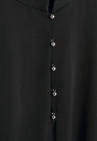 Tissu noir avec une rangée verticale de cinq petits boutons ronds argentés brillants espacés uniformément au centre.