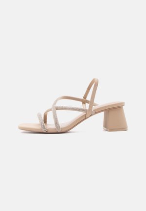 Beige sandal med åpen tå og tykk hæl med tre tynne stropper, to av dem pyntet med små rhinestones som krysser over foten.