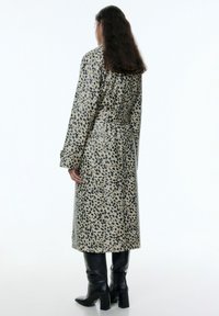 Leopardprint trenchcoat in beige en zwart, met een ceintuur in de taille, lange mouwen en een lengte tot op de knie. Glanzende afwerking, gladde textuur.