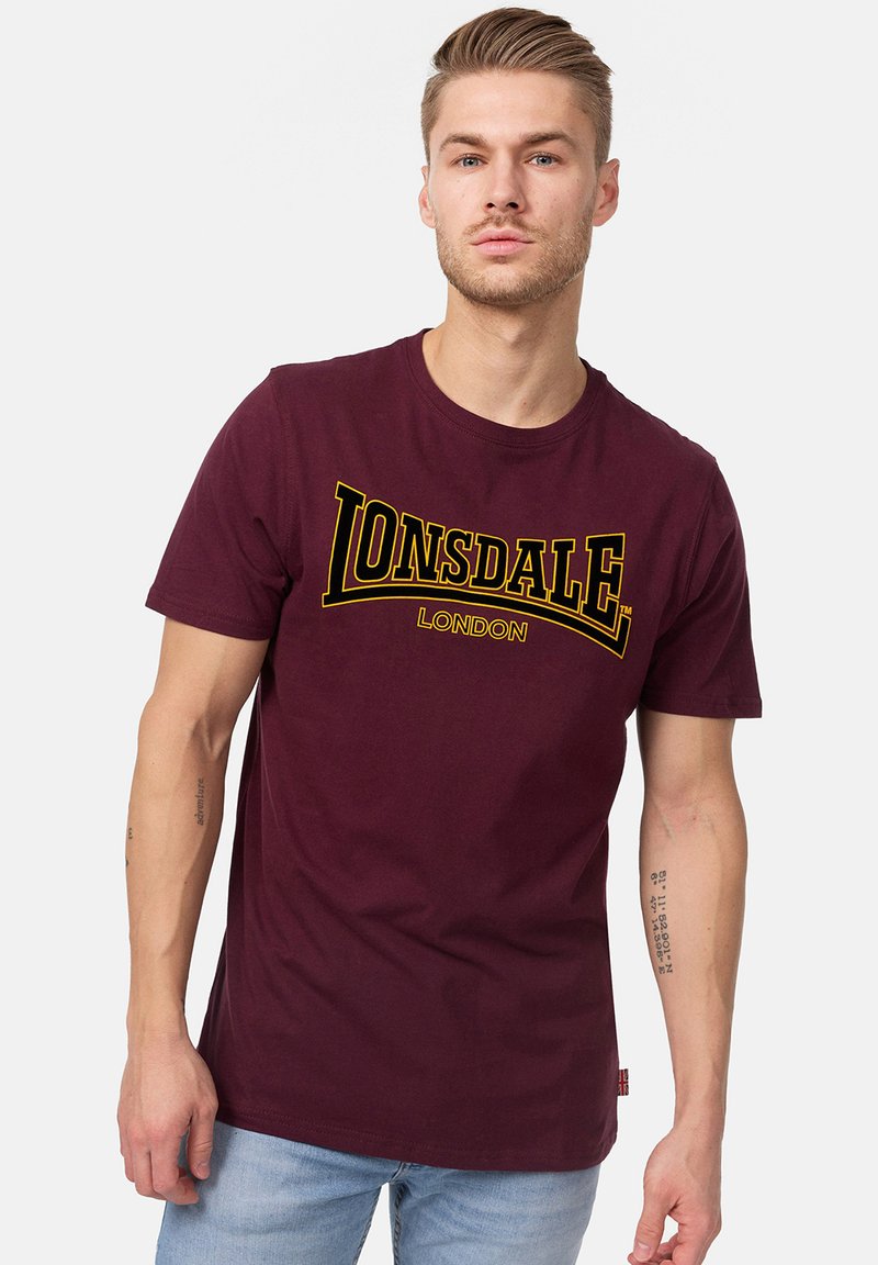 Burgundi színű pamut póló, sárga Lonsdale London logóval. Rövid ujjú, kerek nyakkivágással, sima, puha tapintással.