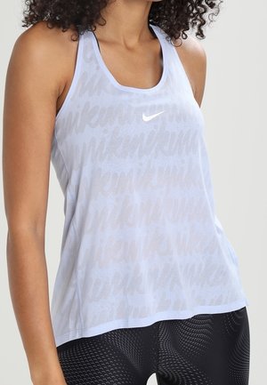 Kvinde iført lyseblå Nike ærmelløs træningstop med subtilt gentaget logomønster og sorte leggings med mønster.