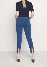 Jeans de denim azul de cintura alta con un corte ajustado, que cuentan con cremalleras en los tobillos y bolsillos traseros. Combinados con botines de tacón en un tono rosa claro.
