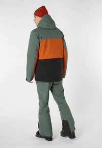 Hooded jack in groene, oranje en zwarte kleurvlakken; gecombineerd met bijpassende groene broeken. Heeft een gladde textuur en een minimalistisch ontwerp.