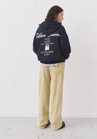 Námornícka mikina s kontrastným bielym textom a grafikou na chrbte, skombinovaná s textúrovanými, svetložltými kordovými nohavicami s širokými nohavicami.
