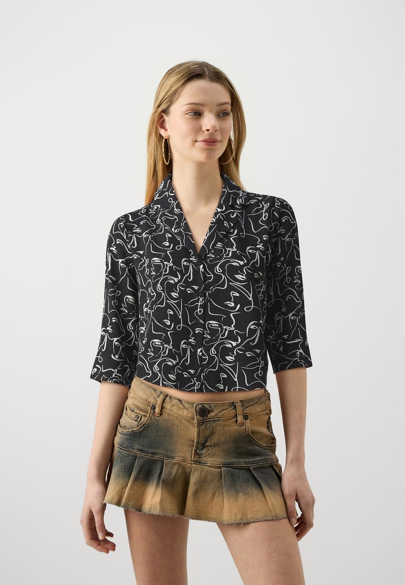 Zwarte crop shirt met een wit abstract lijntekening patroon, voorzien van een kraag en driekwartmouwen, gecombineerd met een lichtbruine denim rok.